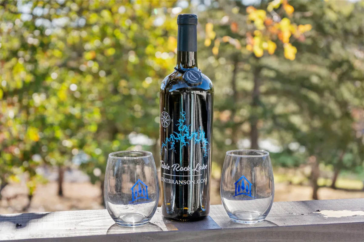 A close-up of a bottle of wine and two glasses set outdoors, suggesting wine tasting or a quiet moment of relaxation surrounded by nature’s backdrop.