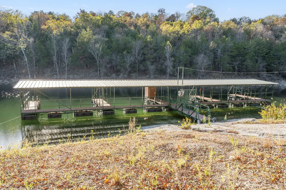 A tranquil view looking out over a dock surrounded by shimmering water and leafy trees. The setting sun casts a golden glow, inviting guests to fish, relax, or simply enjoy the peacefulness from the dock’s edge.