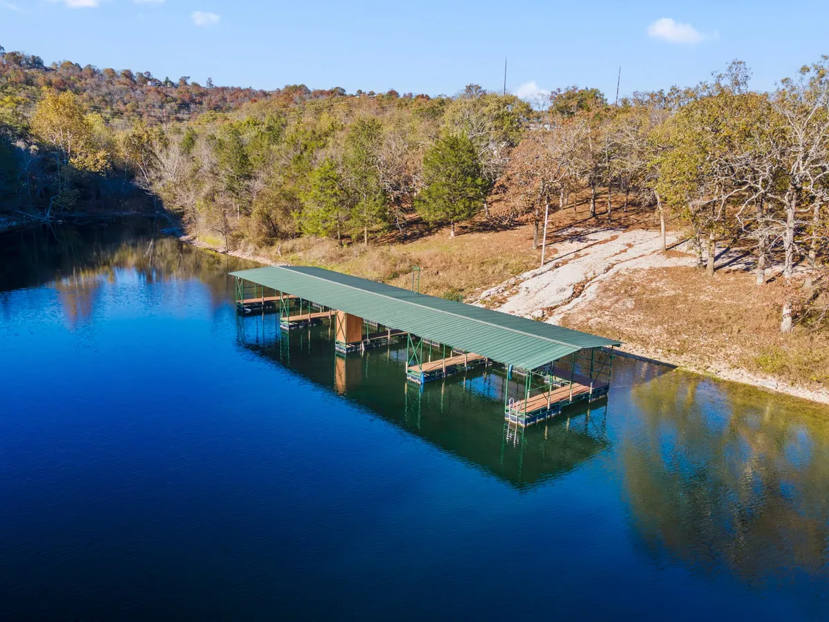 A tranquil boat dock extends over calm, reflective water, bordered by lush trees. The scene is peaceful, with hints of fishing gear and boats ready for use, providing easy access to the lake for water activities. The natural setting offers a serene escape for boating, fishing, or simply enjoying the lakeside environment.