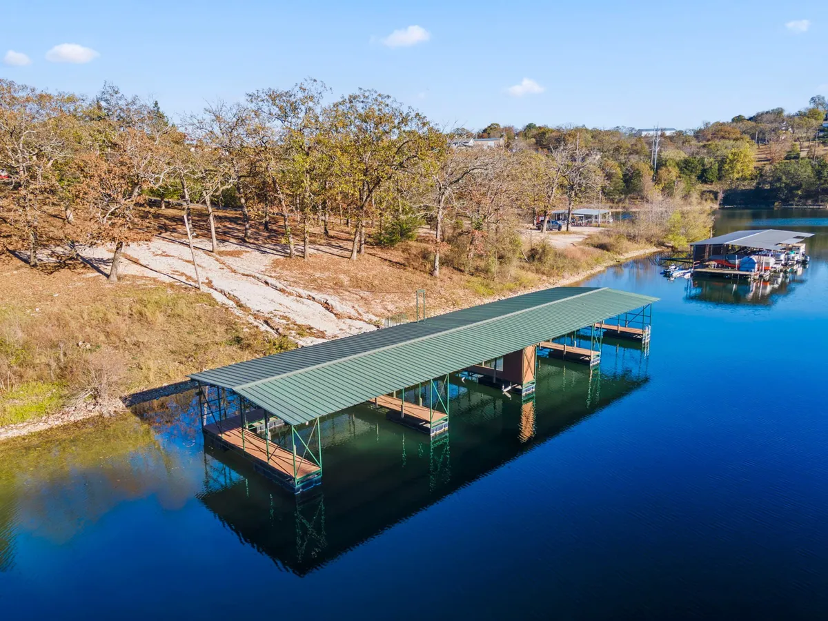 This exterior image features a picturesque boathouse set against calm water and surrounded by lush trees, encapsulating the tranquil lakeside atmosphere of the Table Rock Lake area. The scene suggests recreational activities like boating, fishing, and picnicking close to nature.