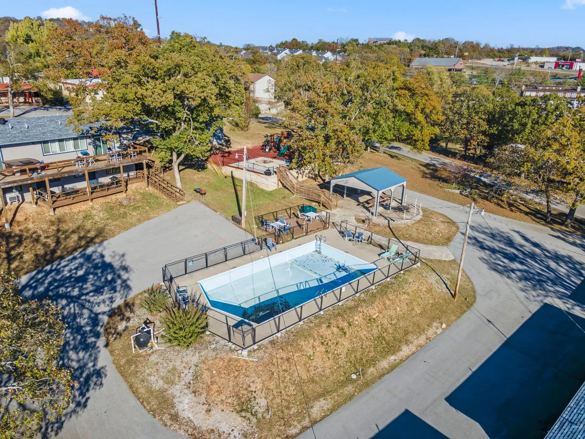 A sparkling swimming pool sits at the heart of the resort, surrounded by lush greenery and a spacious patio area. Lounge chairs and umbrellas invite families to relax, while the pool offers room for swimming and play. The setting feels welcoming and lively, perfect for summer fun and social gatherings.