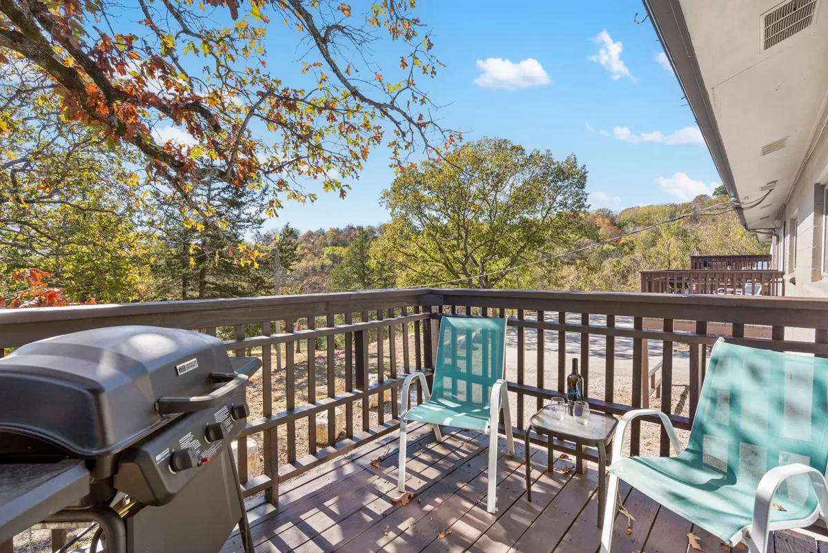A tranquil outdoor area featuring a grill, two chairs, a small table, and lush greenery. The space is ideal for outdoor relaxation, barbecuing, and spending time with family, friends, or pets in nature.
