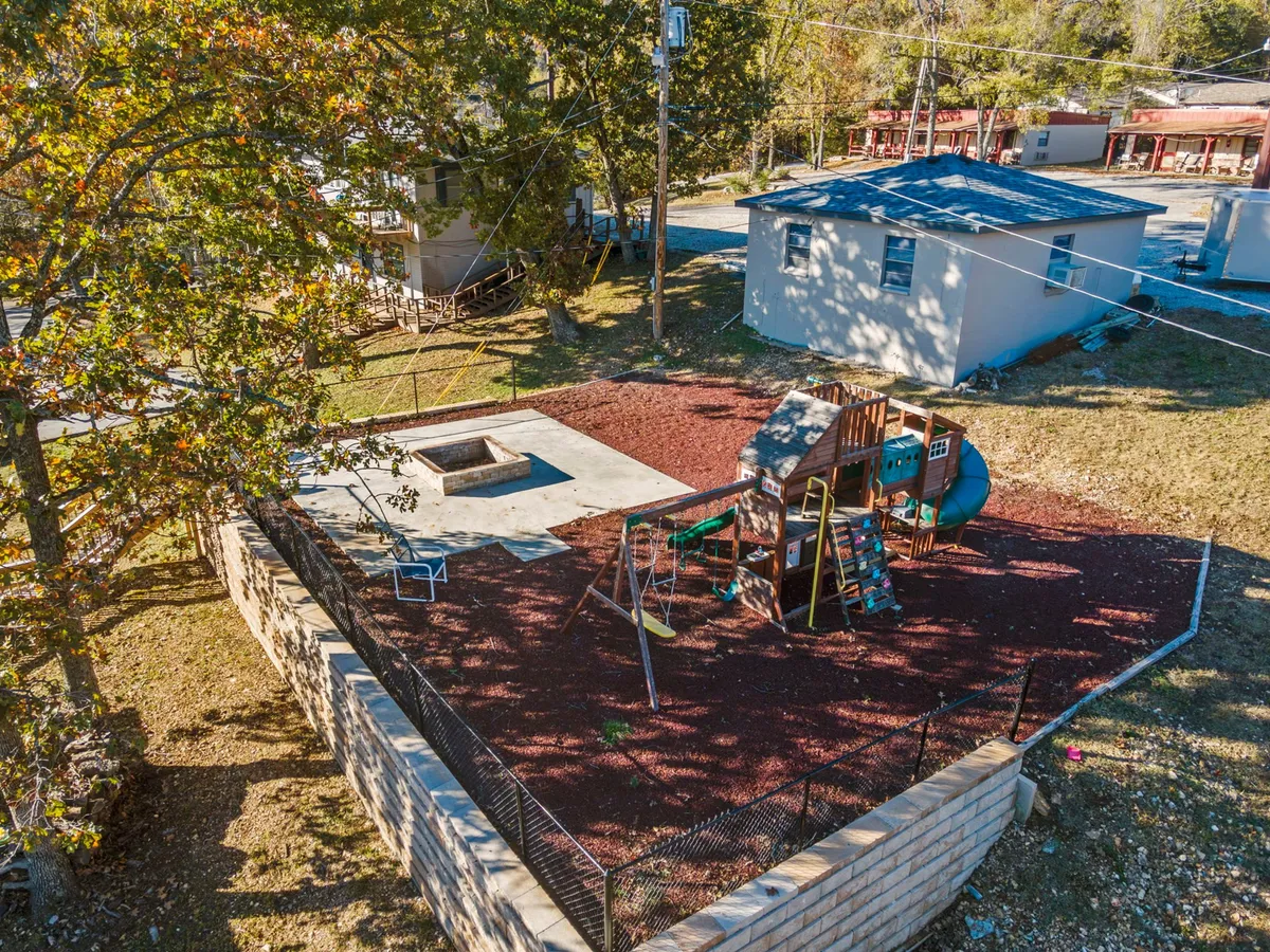 A lively outdoor amenity area featuring colorful playground equipment and a fire pit, set within a safe, fenced-in space. The playground is designed for kids, while the fire pit area encourages gatherings for s’mores and social evenings. The surrounding greenery adds to the inviting, family-friendly ambiance.