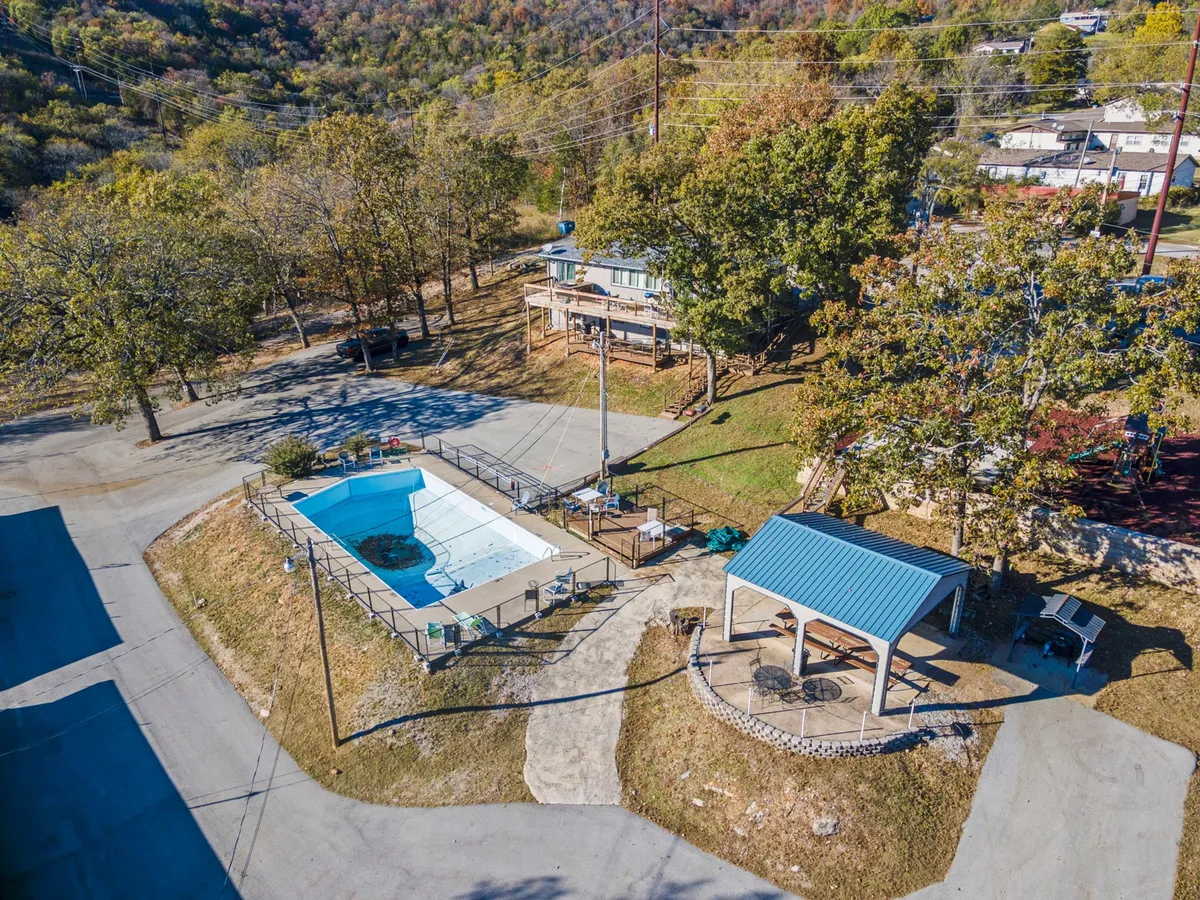 An expansive outdoor area features a swimming pool, a shady gazebo, and mature green trees, creating a setting ideal for group activities. The pool is surrounded by ample deck space for lounging, while the gazebo provides a cozy spot for barbecues or evening gatherings with friends and family.