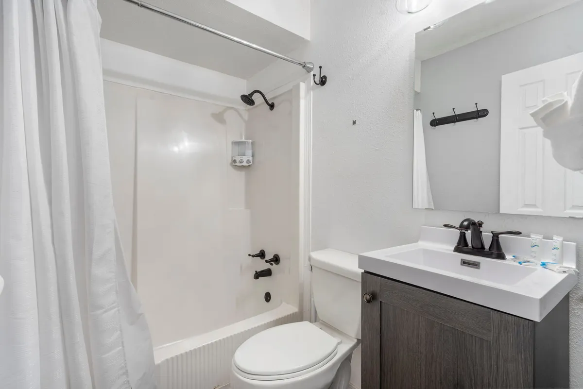 A clean and modern bathroom featuring a shower area, sink with mirror, and toilet. The minimalist design and tidy appearance underscore the emphasis on cleanliness and comfort.